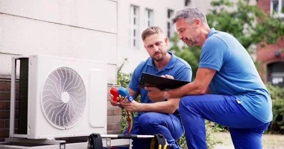 Two technicians discussing an outdoor air conditioning system with gauges and a tablet
